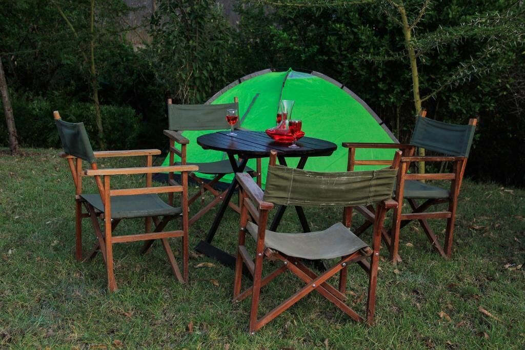 Un coin camping avec une tente verte, une table ronde et quatre chaises en bois.