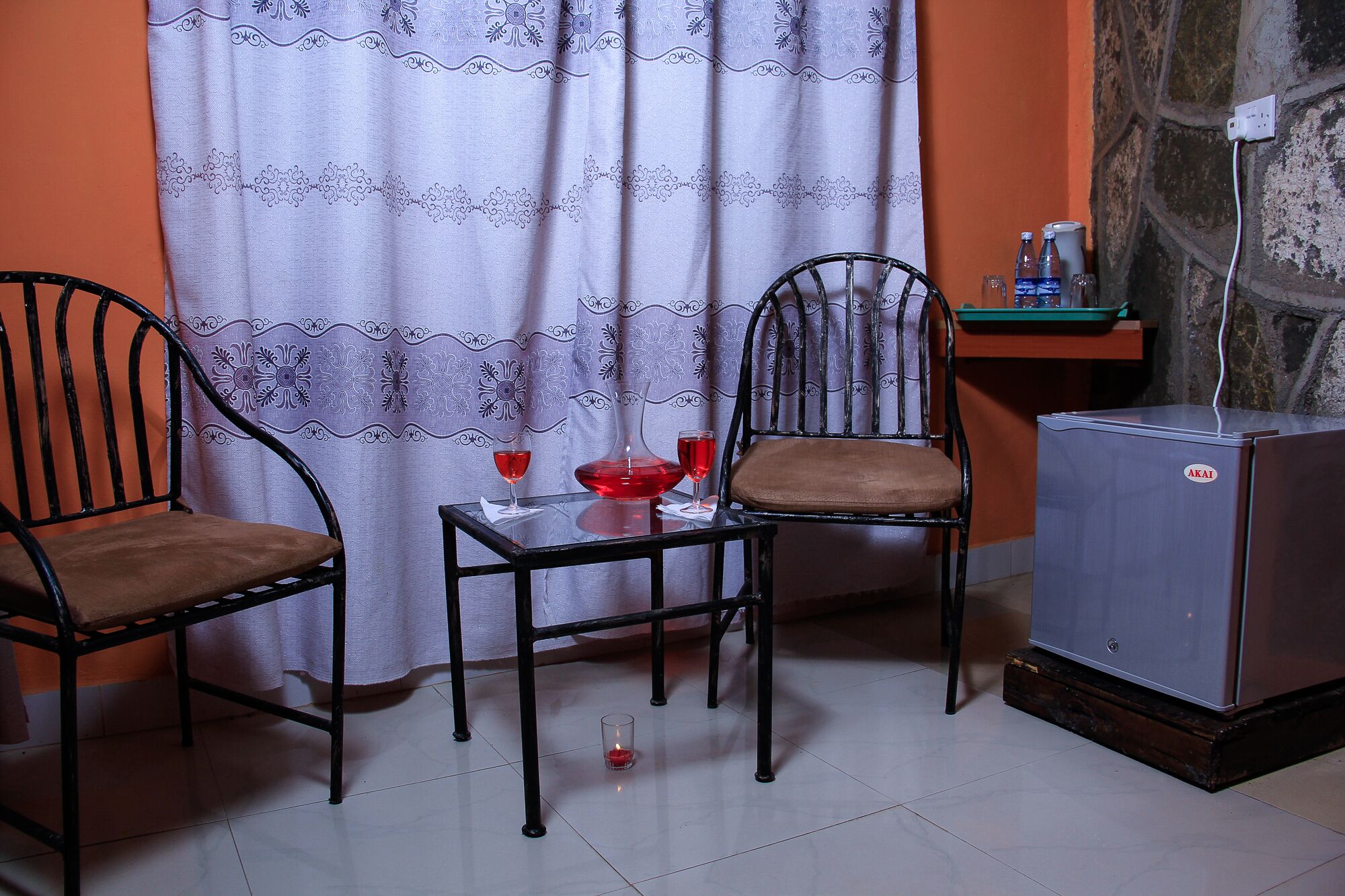 A small room with two chairs, a table, a refrigerator, and a curtain.
