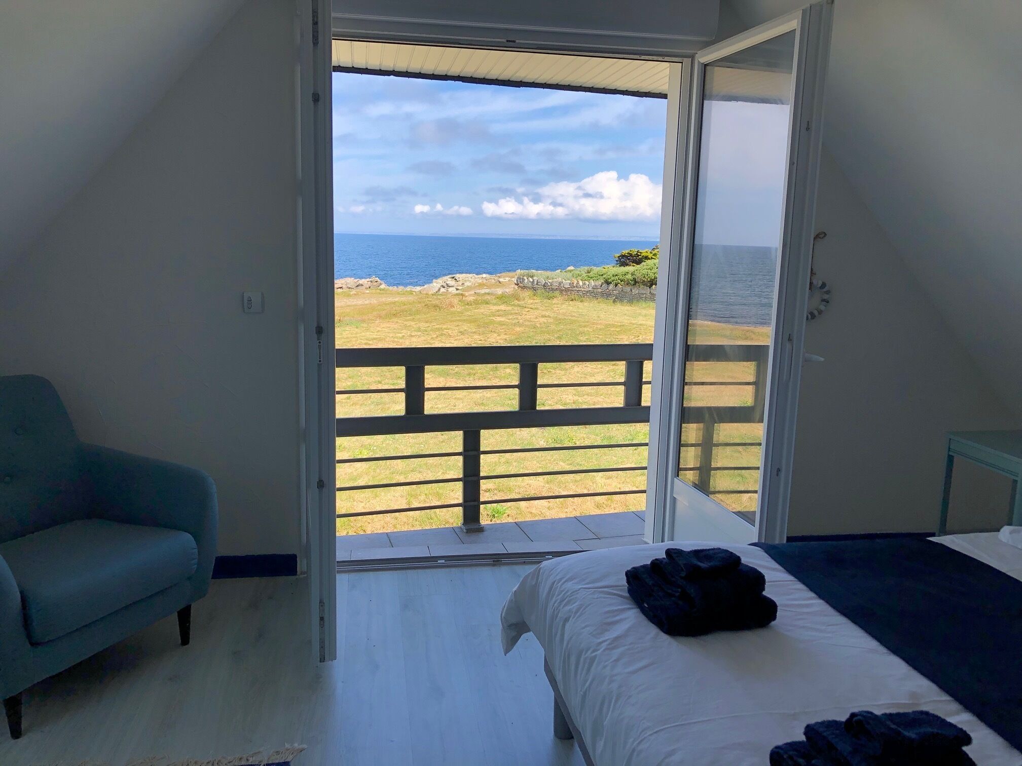 A bedroom with a bed, a sofa, and a view of the sea through an open door.