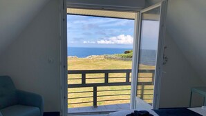A bedroom with a bed, a sofa, and a view of the sea through an open door. - Maison vue mer côte sauvage pointe de la Torche (Penmarch)