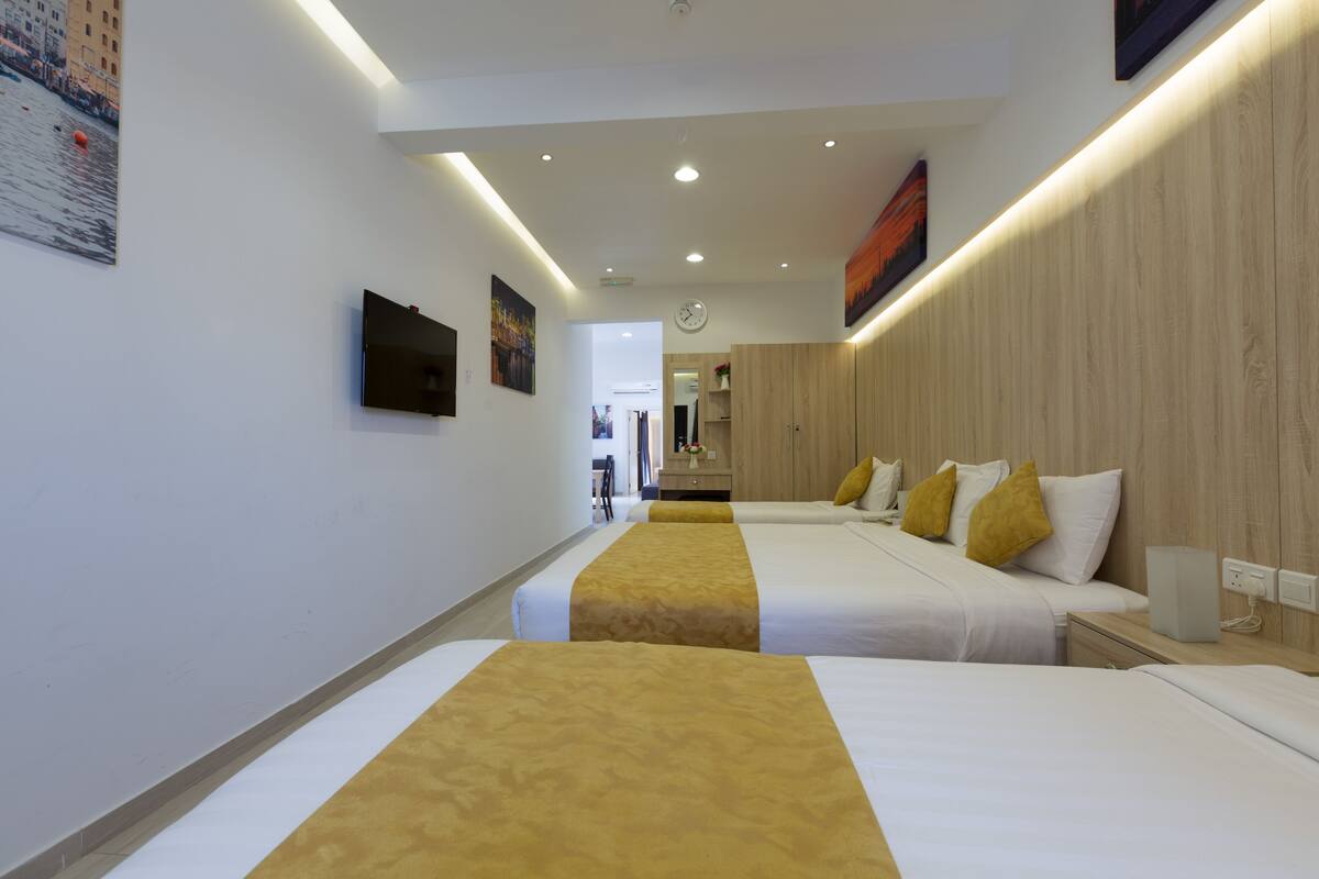 Een hotelkamer met twee bedden, een houten hoofdbord, een flatscreen televisie en een klok aan de muur.