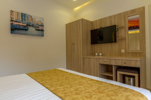 A hotel room with a bed, a TV mounted on a wooden cabinet, and a painting of a cityscape on the wall. - 24 Gold Hotel (Dubai)