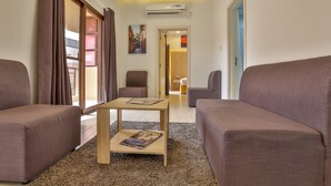 Ein modernes Wohnzimmer mit Sofa, Couchtisch und Blick auf eine Stadtlandschaft durch ein großes Fenster.