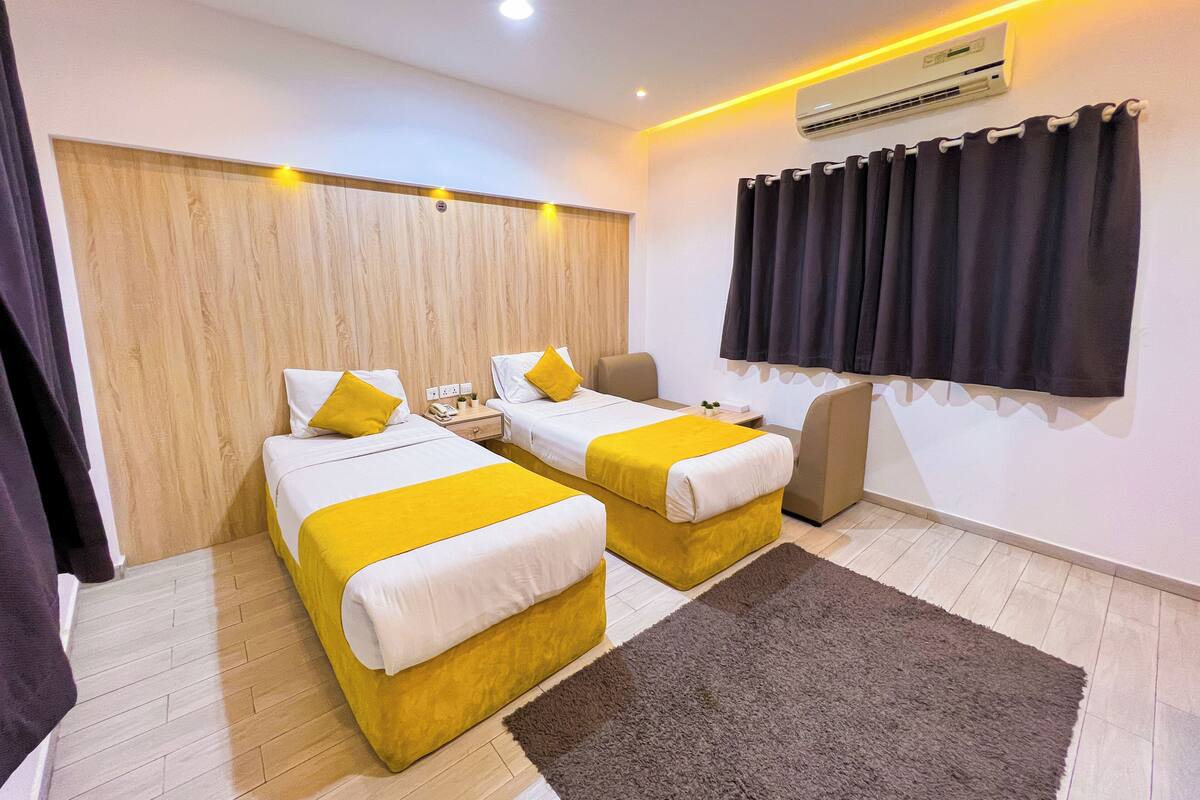 Een hotelkamer met twee bedden, een bureau, een stoel, een vloerkleed, een airconditioner en gordijnen.