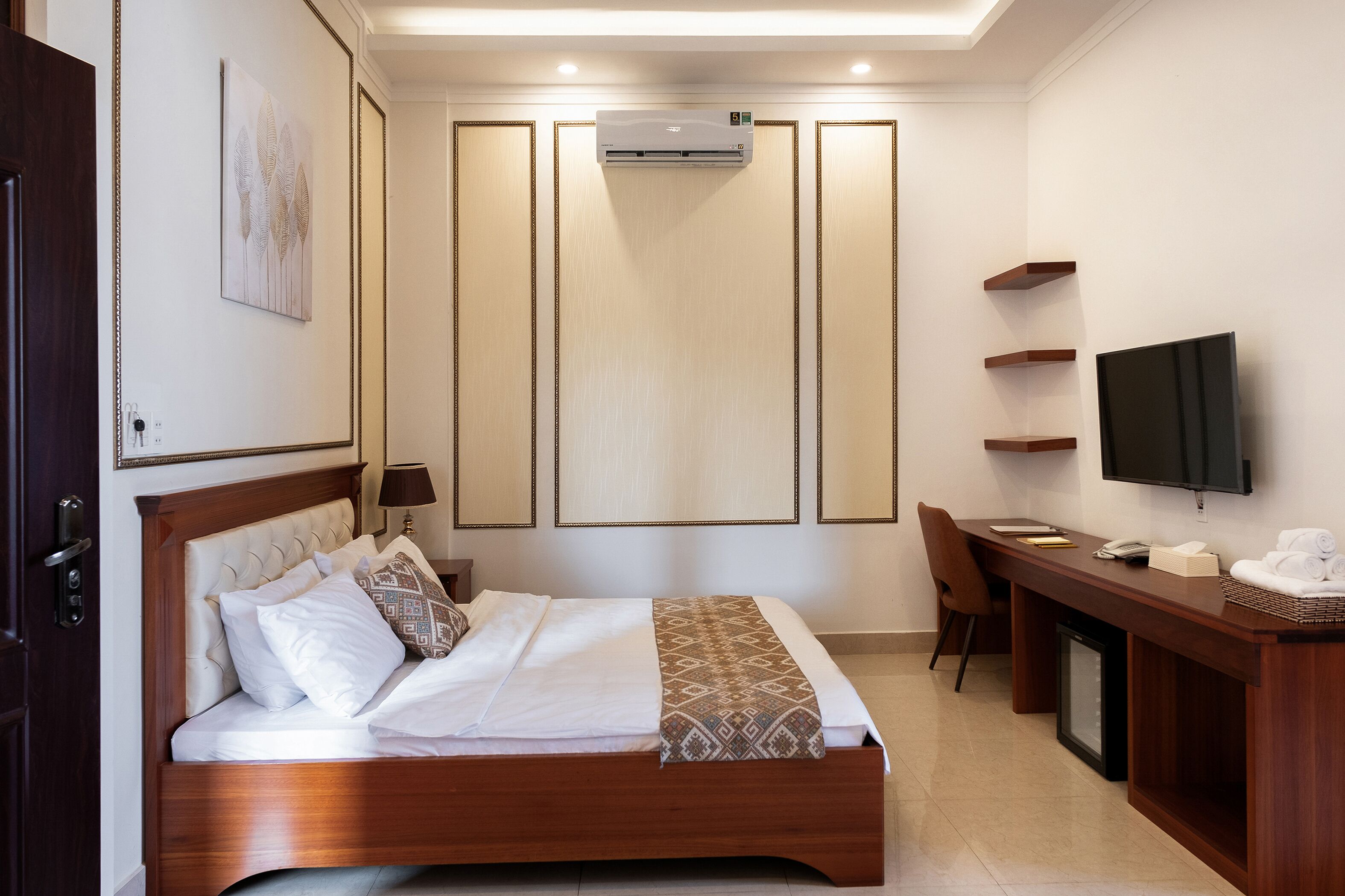 A hotel room with a bed, bedside table, TV, and a desk with a chair.