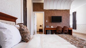 Een hotelkamer met een groot bed, een bureau met twee stoelen, een flatscreen televisie en een kamerkleed met een patroon.