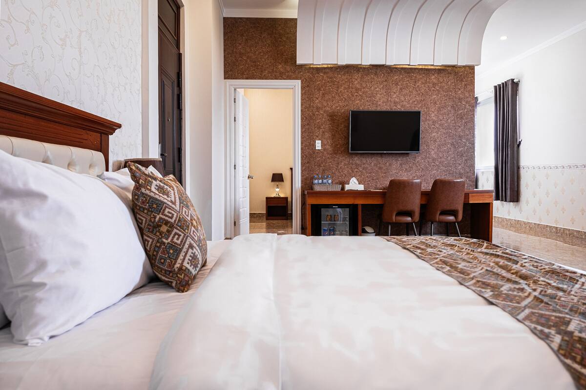 Une chambre d’hôtel avec un grand lit, un bureau avec deux chaises, un téléviseur à écran plat et un tapis à motifs.