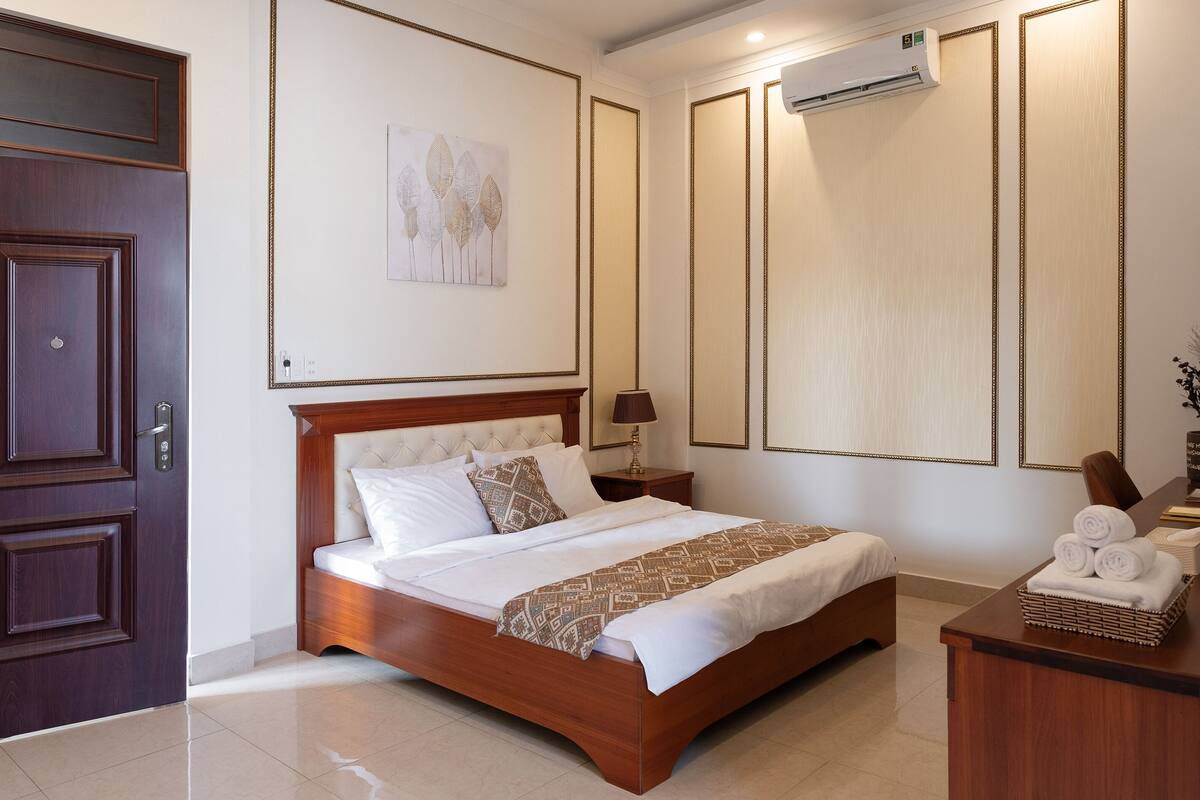 Une chambre à coucher bien rangée, avec un lit en bois, une table de chevet avec une lampe et un climatiseur fixé au mur.