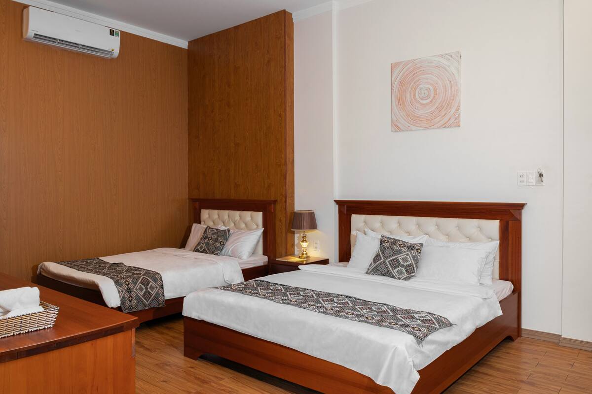 Une chambre d’hôtel avec deux lits, une tête de lit en bois, une table de chevet avec une lampe et un climatiseur fixé au mur.