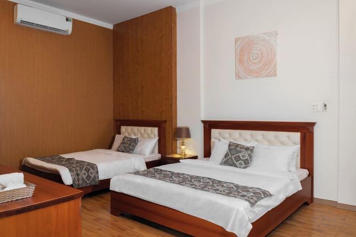 A hotel room with two beds, a desk, and a wall-mounted air conditioner.