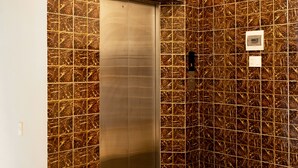 Een lift met een metalen afwerking, omringd door een patroonwand en een marmeren vloer met decoratieve rand.