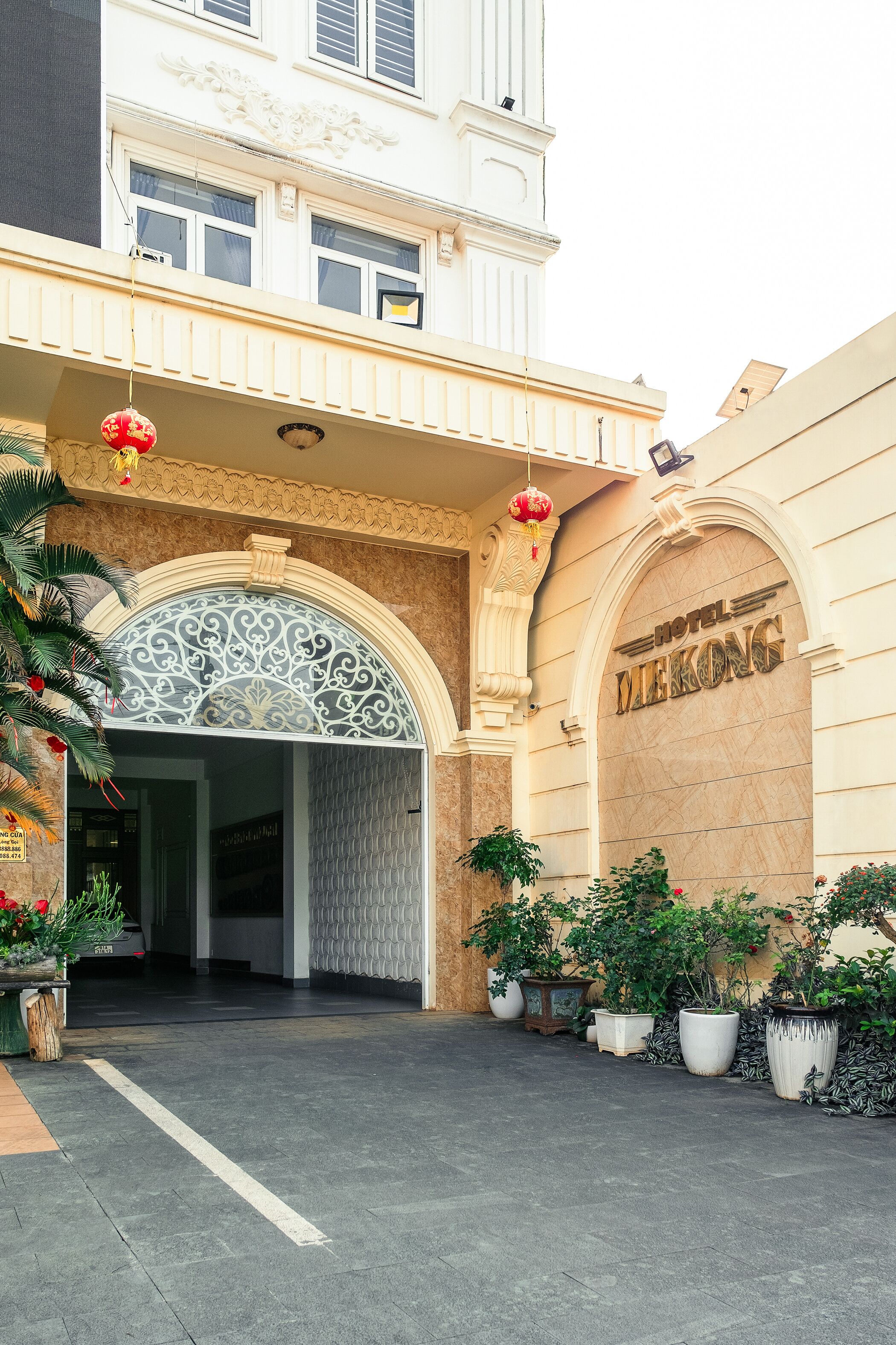 A hotel entrance with a large arched doorway, potted plants, and a sign reading "Hotel Mekong".