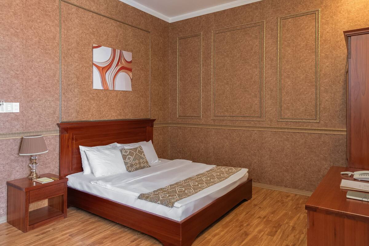 Un lit bien fait, avec une tête de lit en bois, une table de chevet avec une lampe et une œuvre d’art accrochée au mur.
