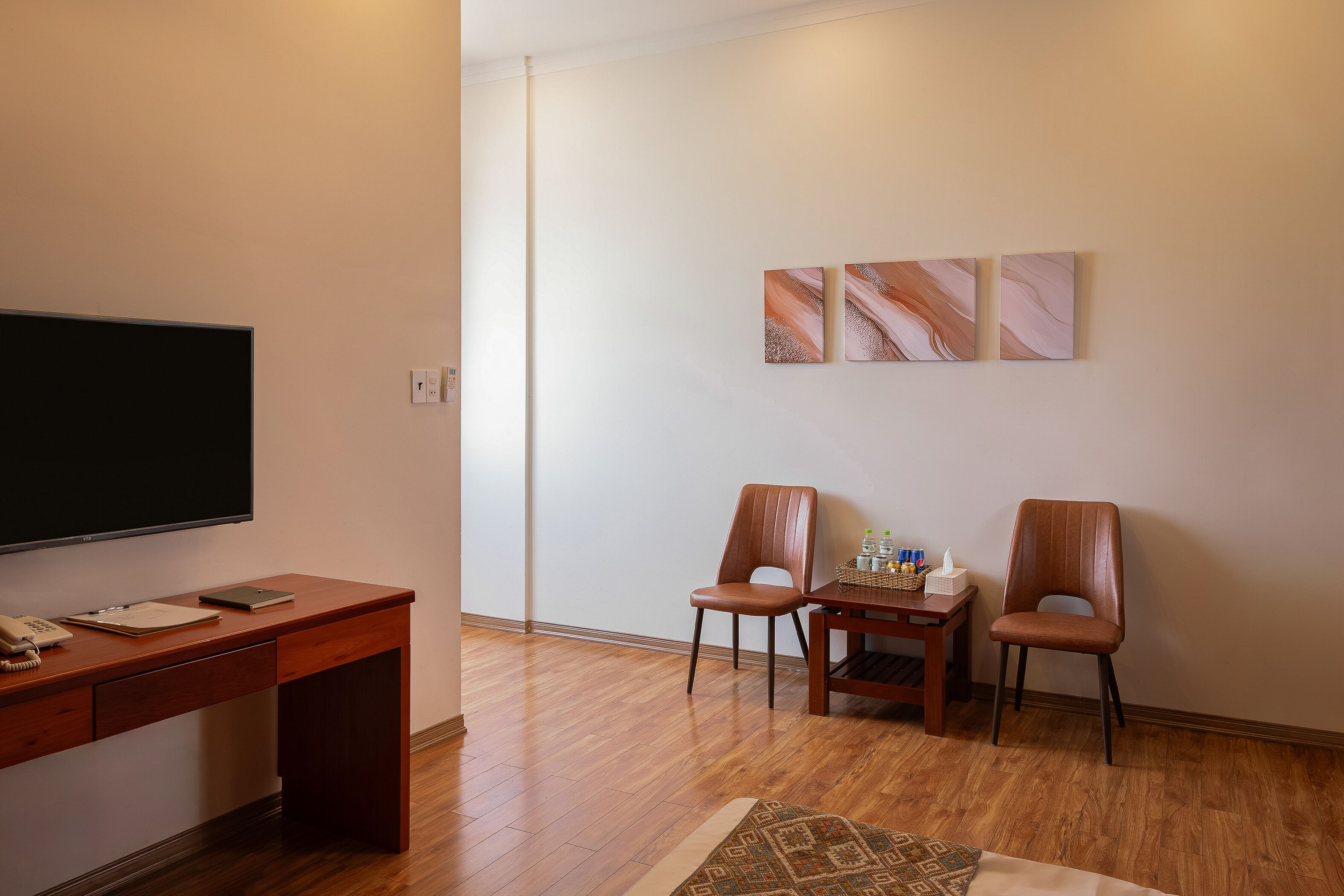 A room with a wooden desk, two chairs, a flat-screen TV, and a small table with a tissue box and bottles.