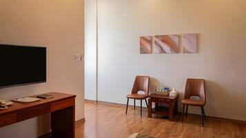 A room with a wooden desk, two chairs, a flat-screen TV, and a small table with a tissue box and bottles.