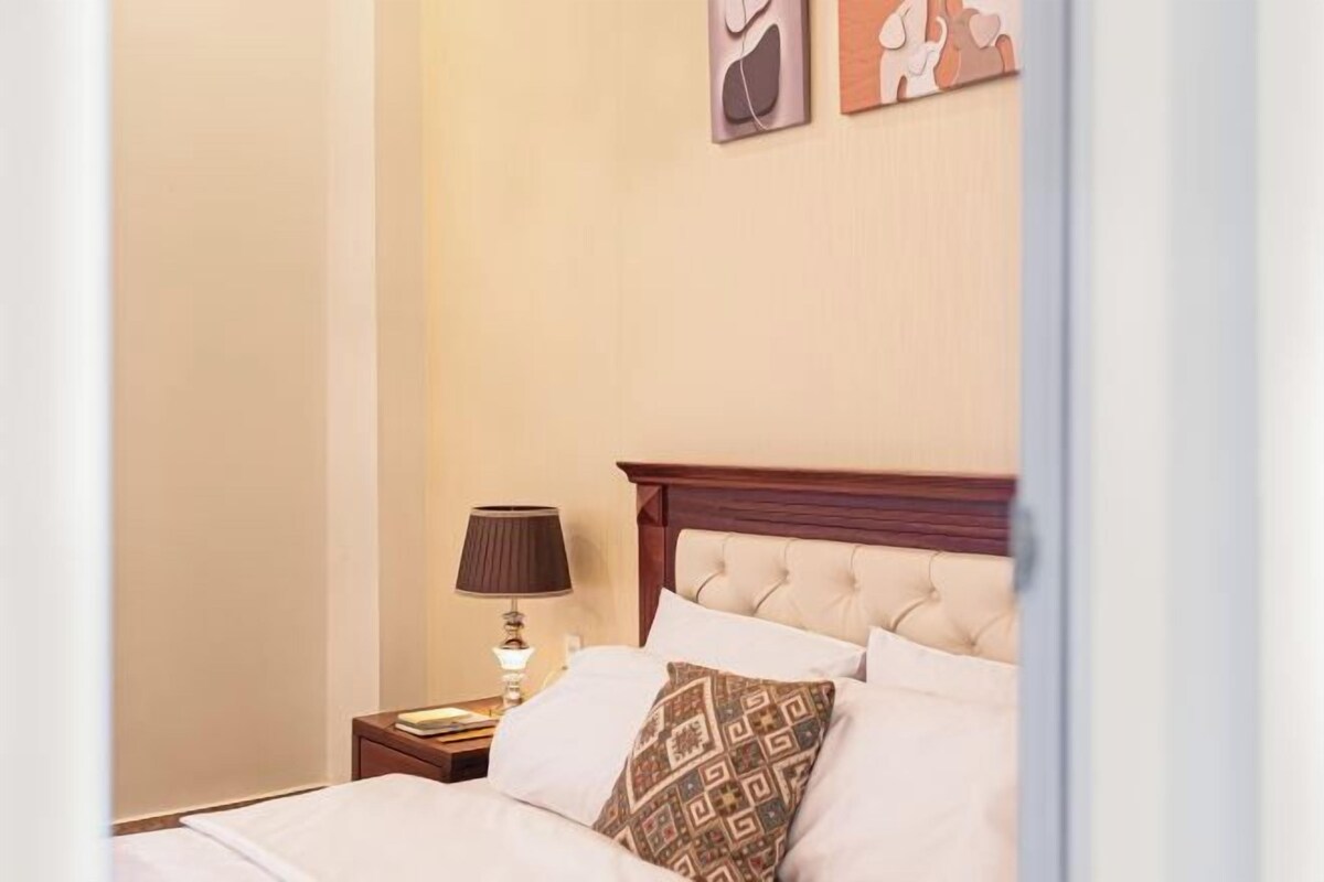 Quarto de hotel com uma cama, mesa de cabeceira, luminária e parede com duas molduras.