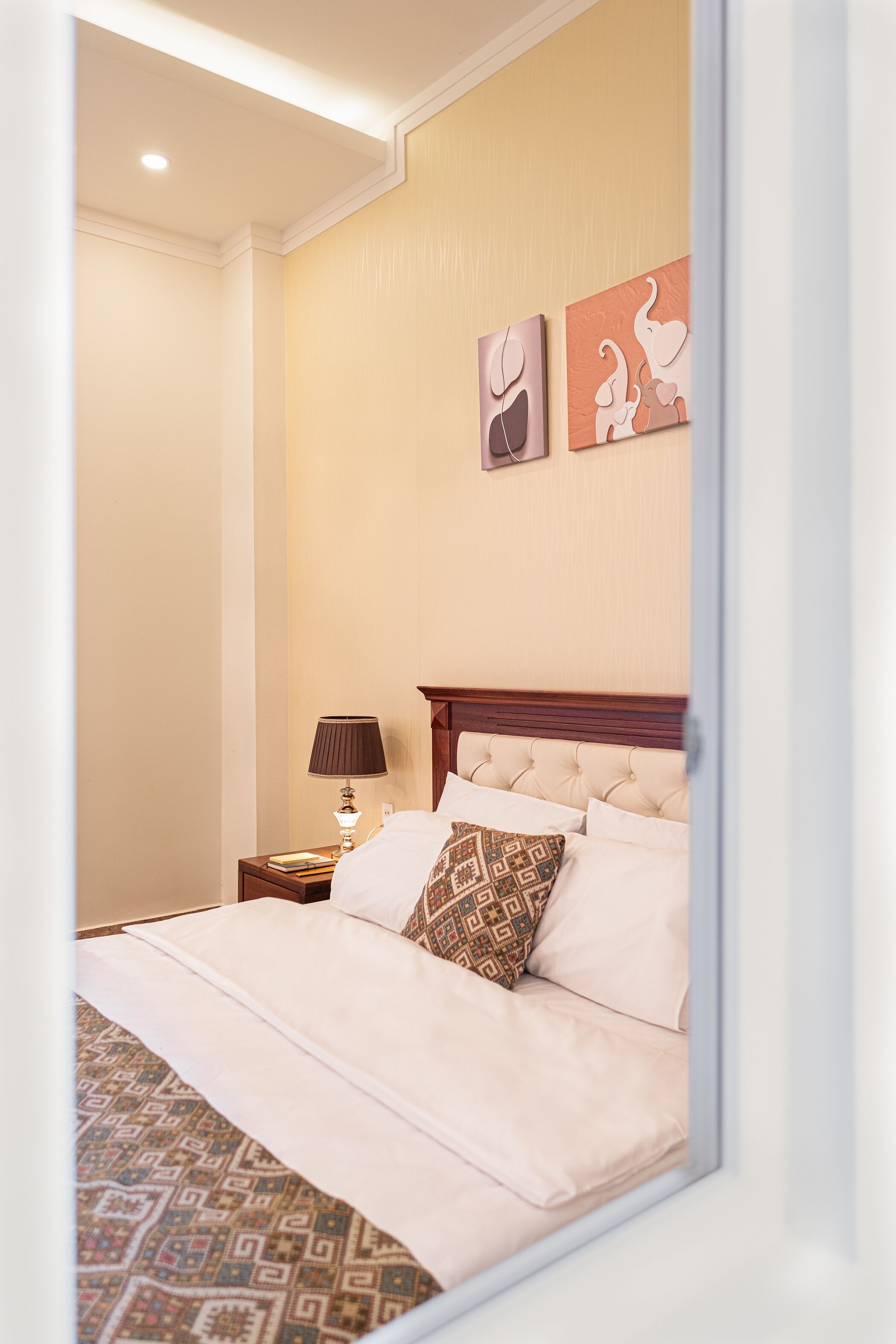 A neatly made bed with a patterned bedspread, a bedside lamp, and two wall art pieces.