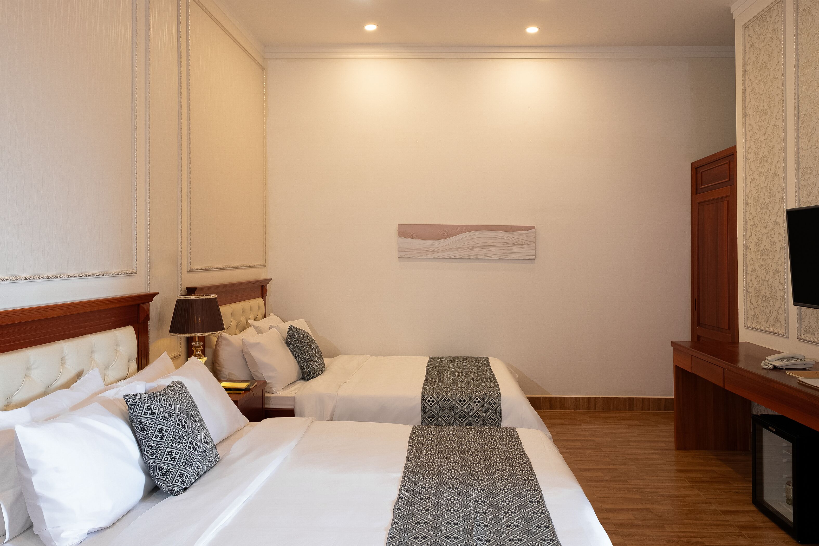 Habitació d'hotel amb dos llits, un escriptori, una televisió i una obra d'art penjada a la paret.
