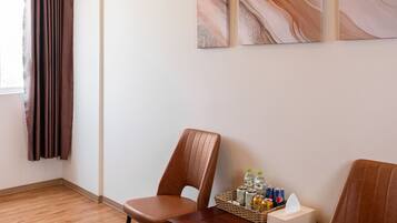 A hotel room with wooden flooring, two brown leather chairs, a wooden table with a basket and bottles, and three abstract paintings on the wall.