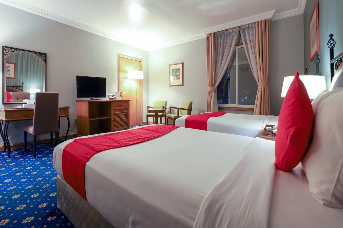 Une chambre d’hôtel avec deux lits, un bureau avec un ordinateur, une télévision et une fenêtre avec des rideaux.