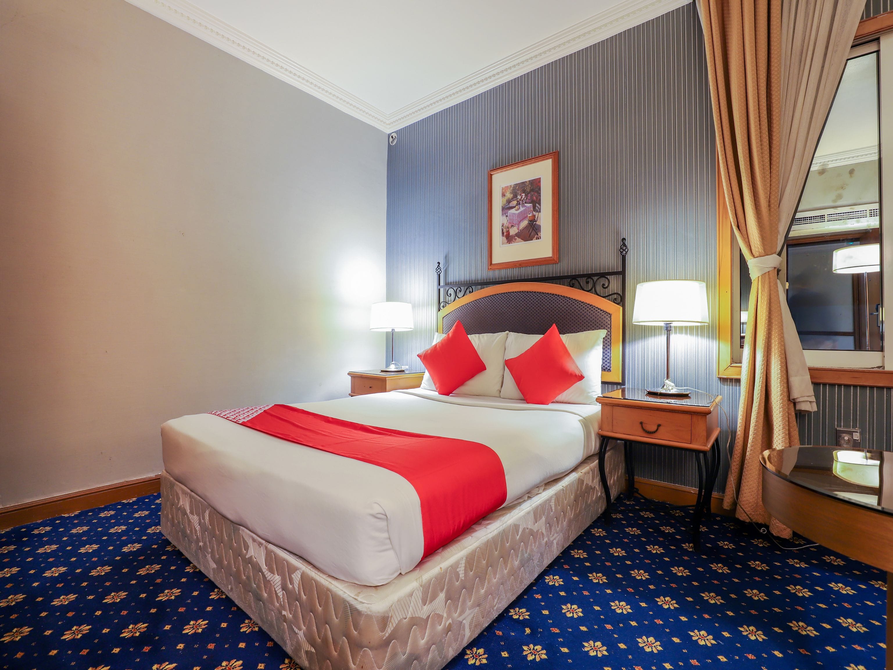 Habitación de hotel con cama, dos mesitas de noche, un tocador, un espejo y una ventana con cortinas.