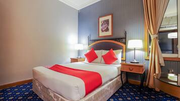 Habitación de hotel con cama, dos mesitas de noche, un tocador, un espejo y una ventana con cortinas.