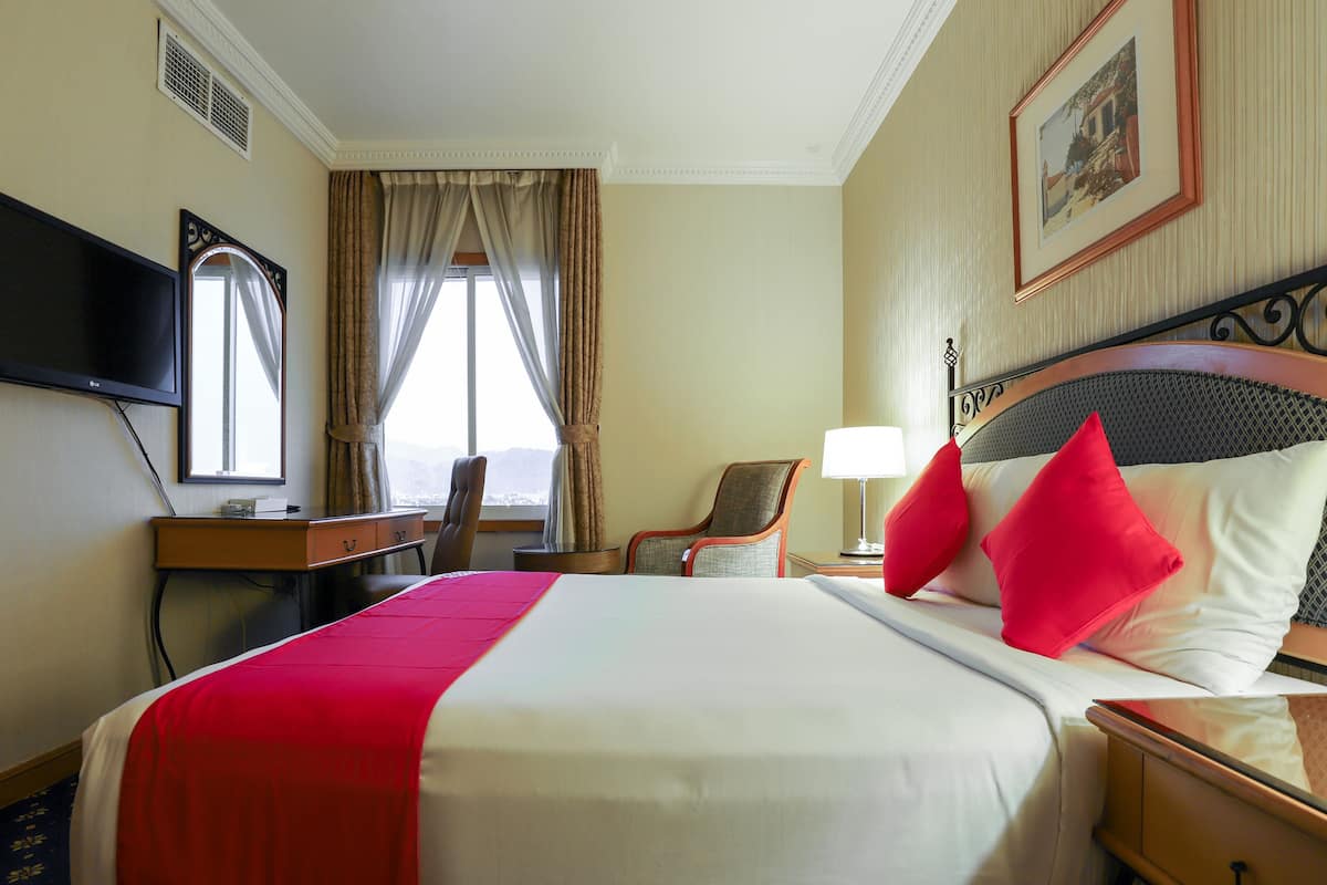 Une chambre d’hôtel avec un grand lit, un bureau doté d’un téléviseur à écran plat, une chaise, une lampe et un tableau encadré au mur.