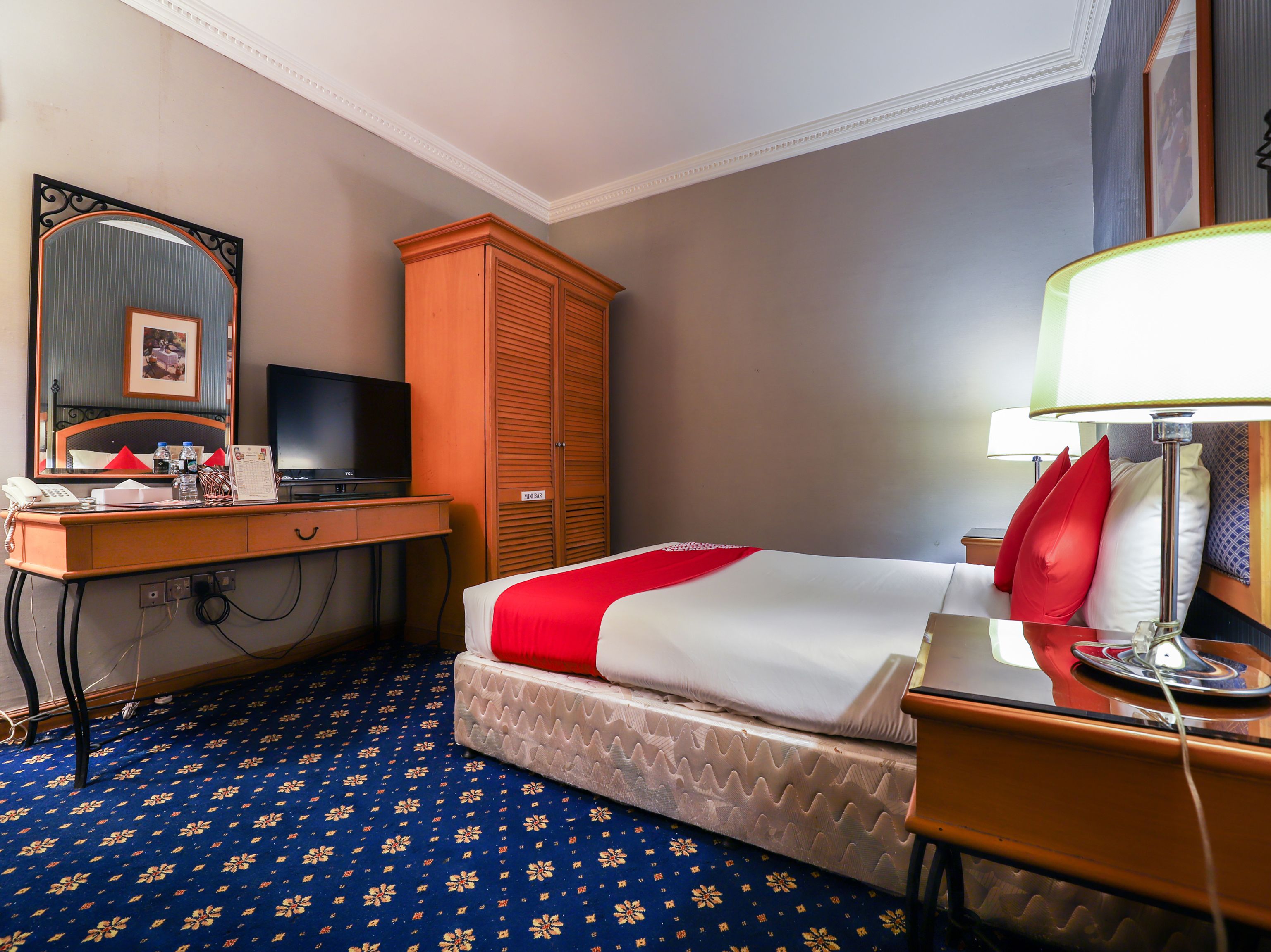 A hotel room with a bed, a desk with a telephone, a television, a wardrobe, and a lamp.