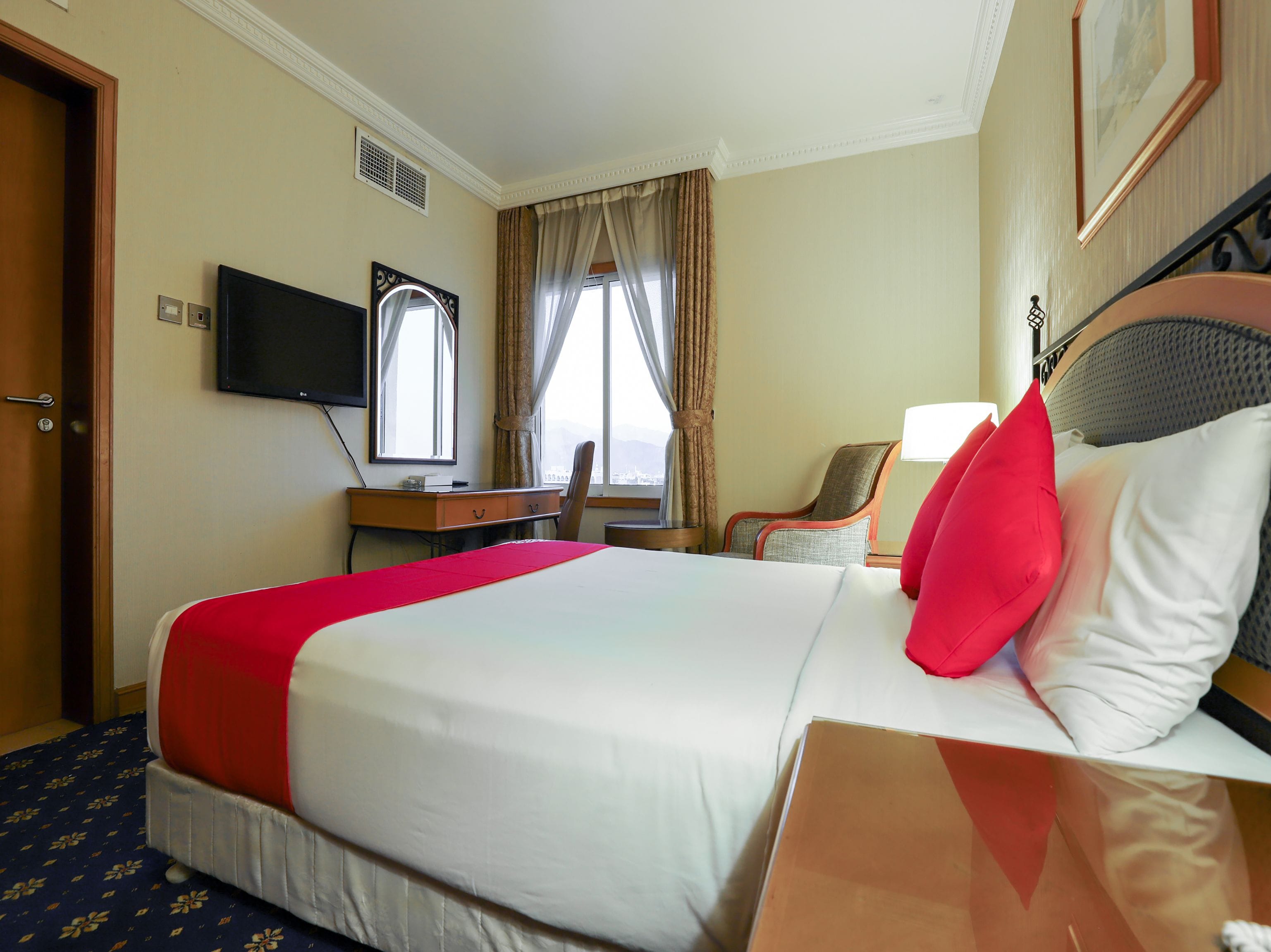 A hotel room with a large bed, a desk with a chair, a TV, and a window with curtains.