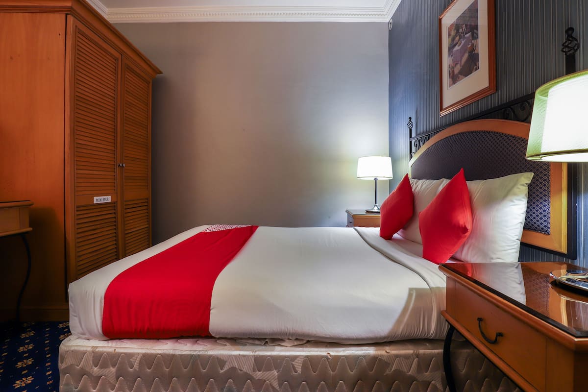 Une chambre d’hôtel avec un lit, une table de chevet, une lampe, un panneau indiquant la présence d’un mini-bar et un grand miroir.