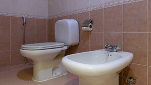 A bathroom with two toilets and a bidet, tiled walls, and a ceiling with a grid pattern. - City Plaza Hotel (Al-Fujairah)