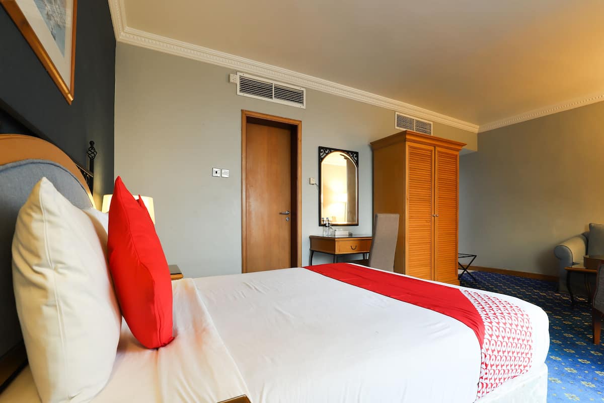 Une chambre d’hôtel comprenant un lit, une armoire en bois, un bureau avec une chaise et un miroir.