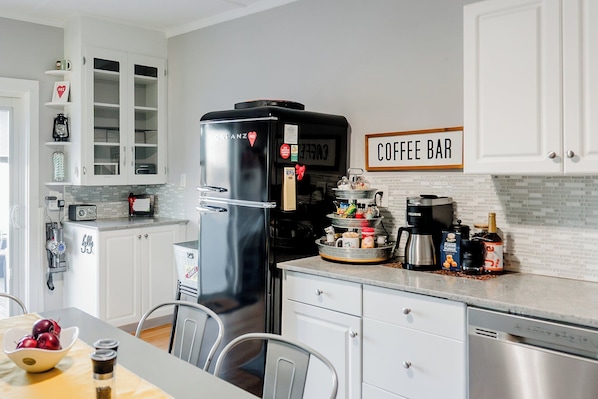 Eine Küche mit weißen Schränken, einem schwarzen Kühlschrank, einem Schild für eine Kaffeebar und verschiedenen Küchengeräten.
