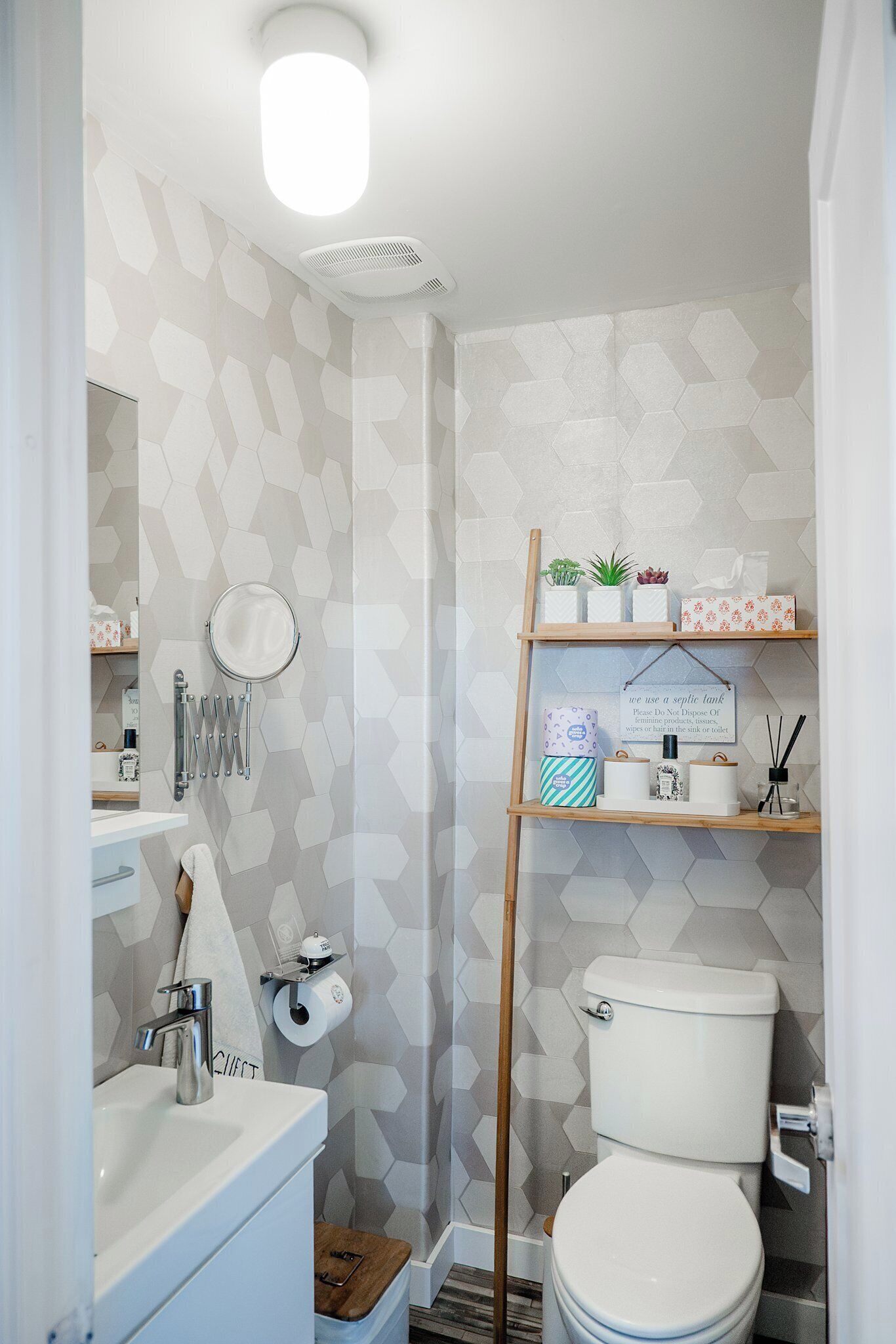 A modern bathroom with a toilet, sink, and shower. There are shelves with toiletries and a mirror.