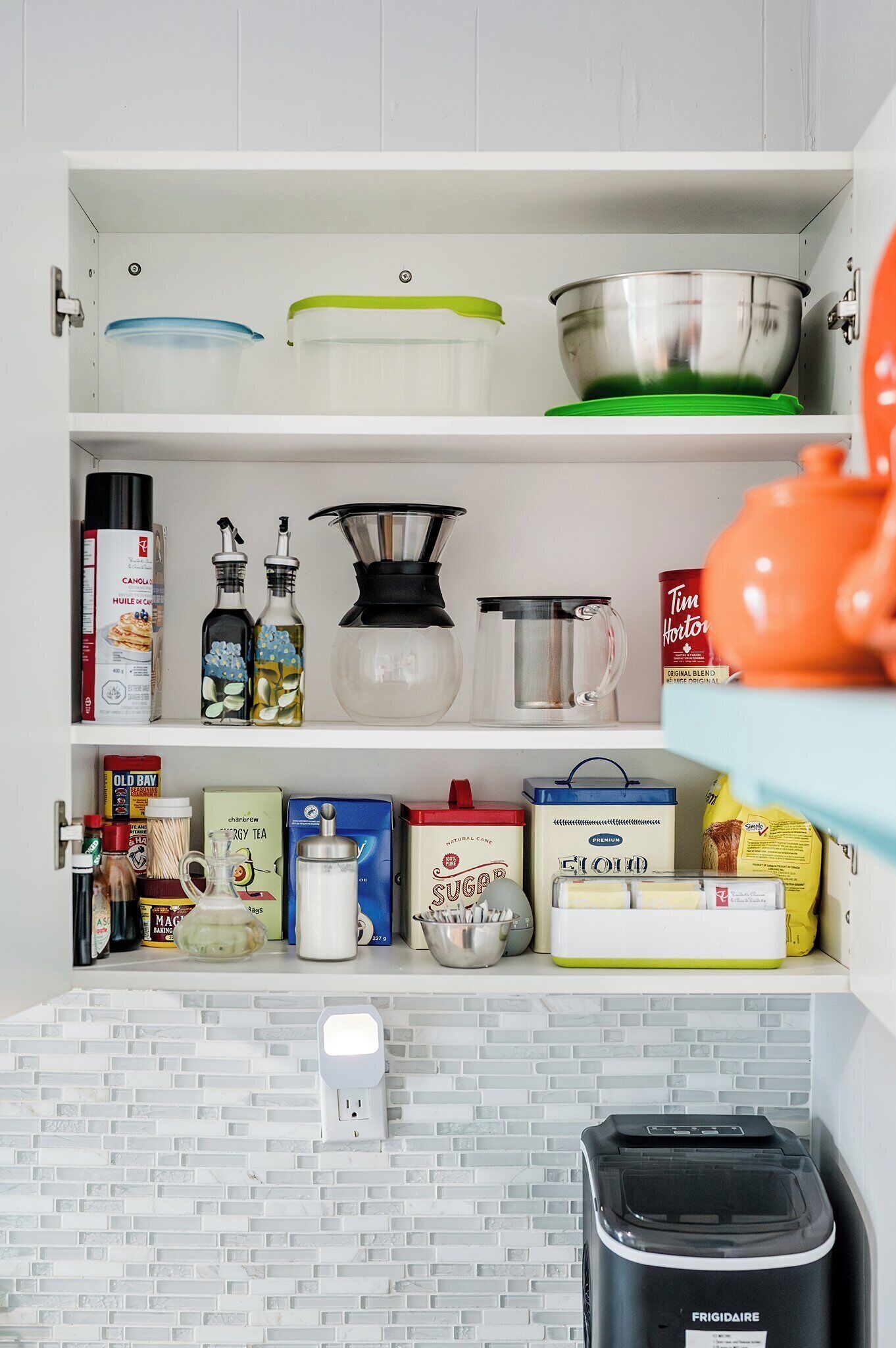 A kitchen with white cabinets, a white tiled backsplash, and a black trash bin labeled "FRIGIDAIRE".