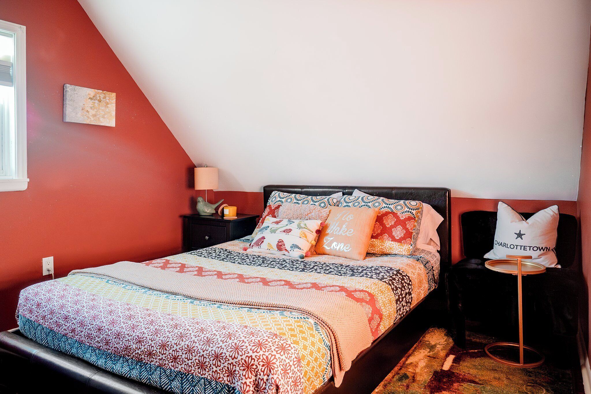 Une chambre à coucher avec un lit, une table de chevet, une lampe, une chaise et un coussin orné de motifs.