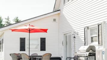 A white house with a barbecue area, outdoor seating with a red umbrella, and a welcome sign.