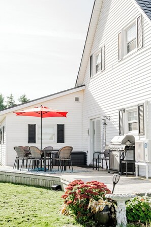 A white house with a barbecue area, outdoor seating with a red umbrella, and a welcome sign.