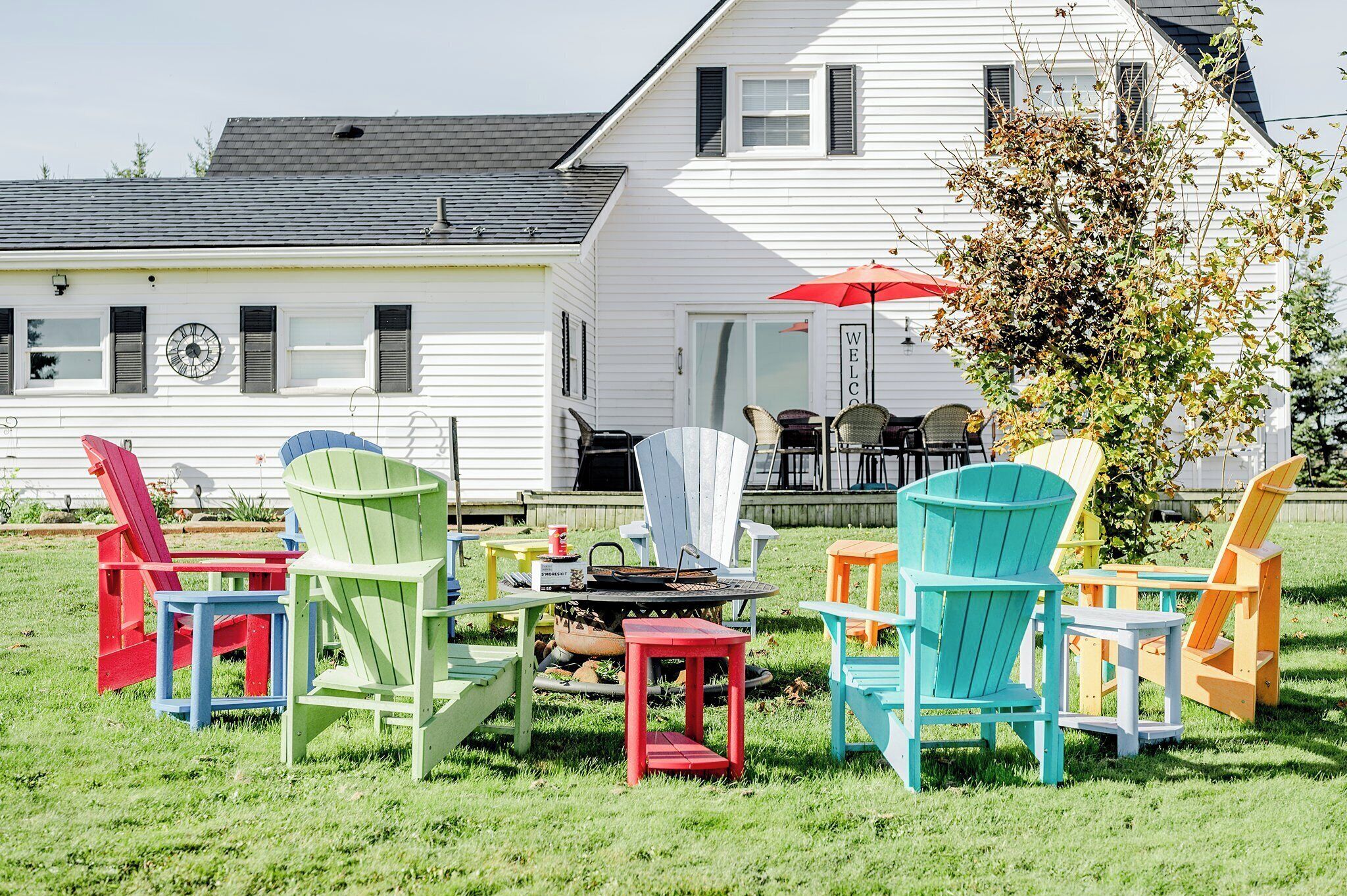 Een groen gazon met kleurrijke Adirondack stoelen en een vuurkuil.