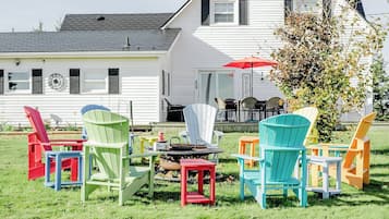 Een groen gazon met kleurrijke Adirondack stoelen en een vuurkuil.