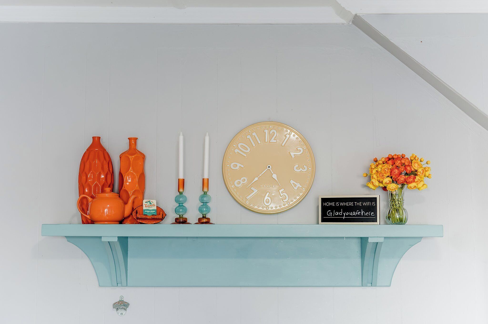 Ein blaugrünes Regal mit einer Uhr, Kerzen, einem Teekessel und einer Blumenvase.