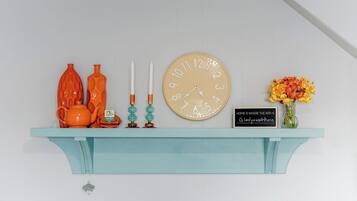 Ein blaugrünes Regal mit einer Uhr, Kerzen, einem Teekessel und einer Blumenvase.