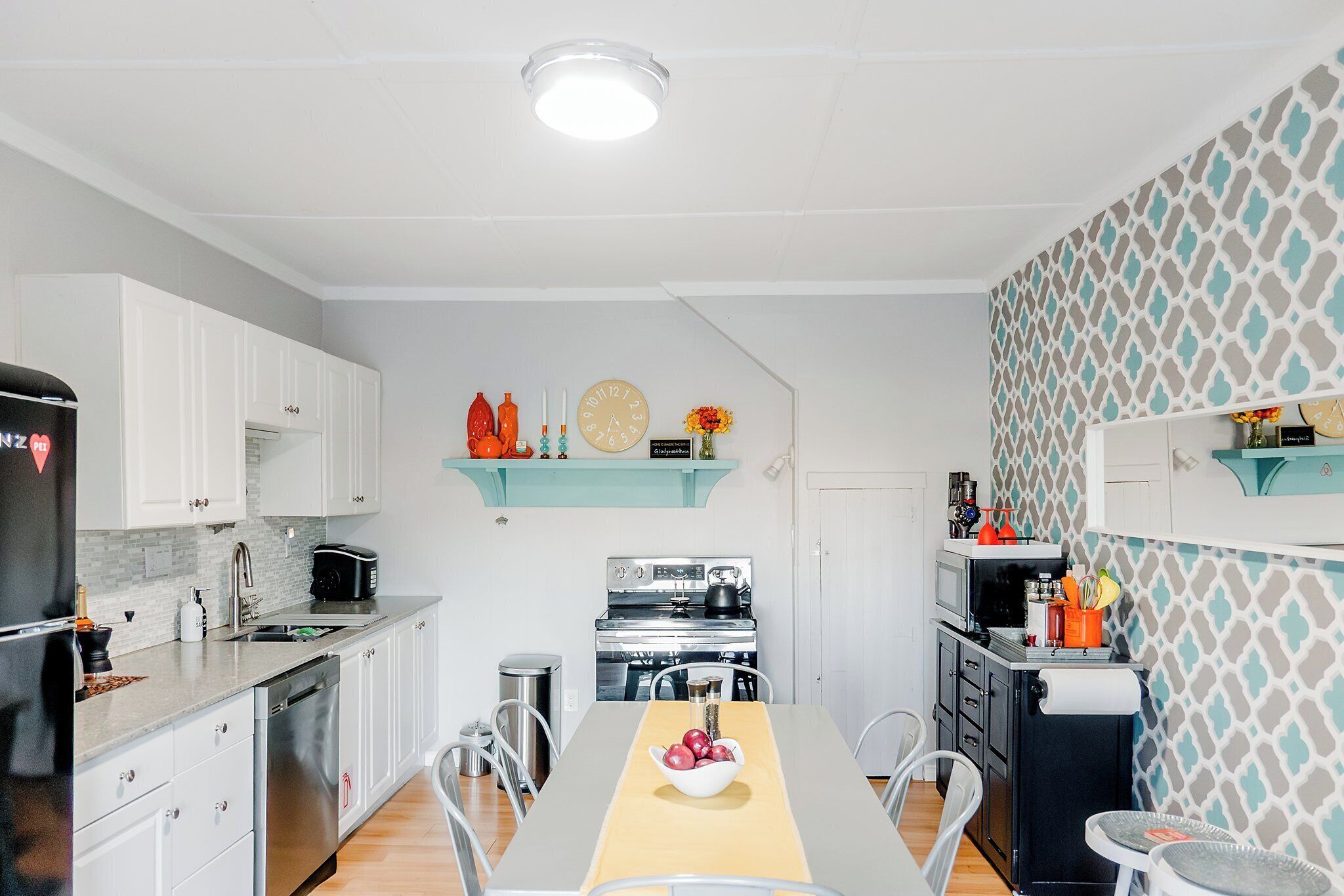 A modern kitchen with white cabinets, stainless steel appliances, and a dining area with a yellow table runner.