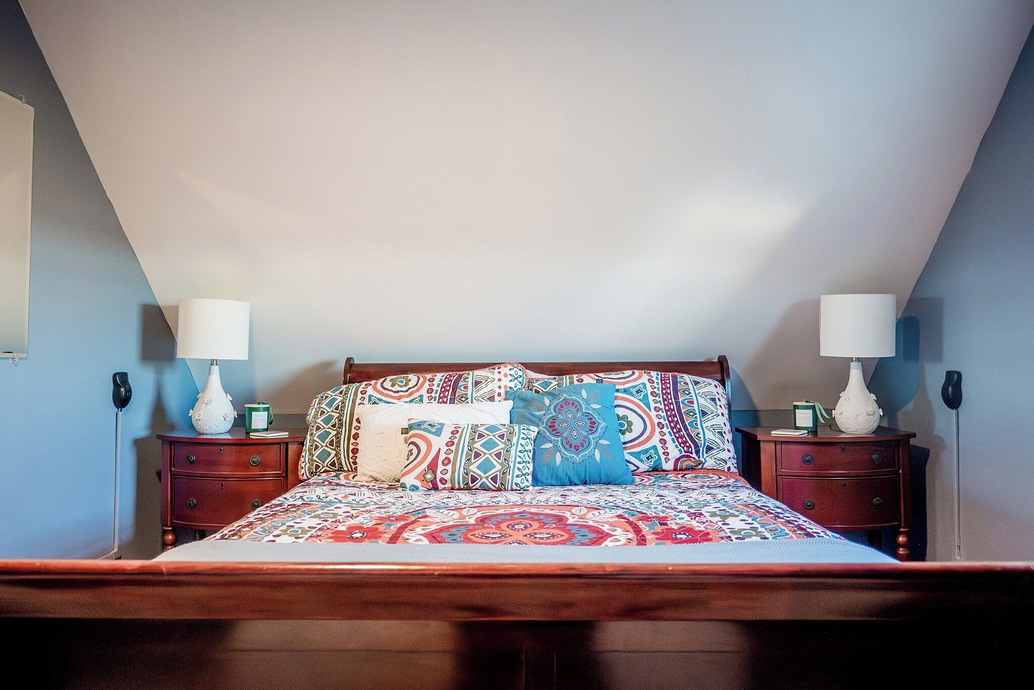 A bedroom with a wooden bed, patterned bedding, two bedside tables with lamps, and a blue wall.