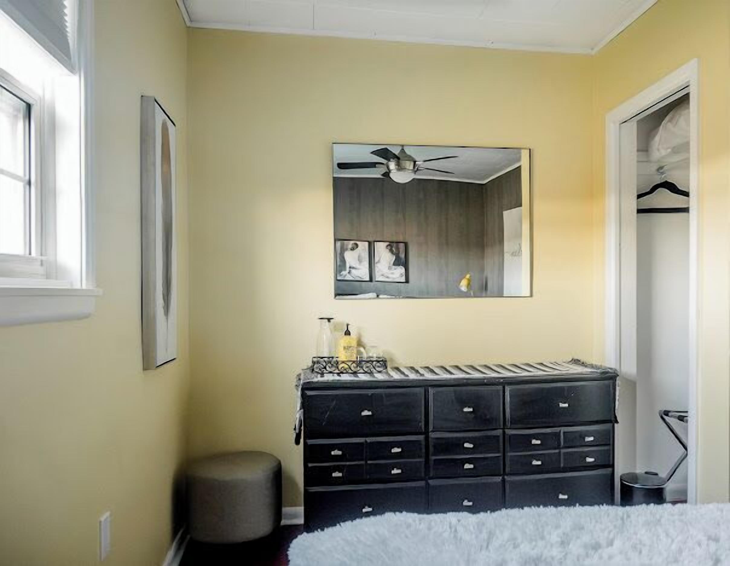A bedroom with a large dresser, a ceiling fan, and a mirror reflecting a ceiling fan.