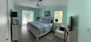 Un dormitorio con cama, escritorio, silla, televisor y ventilador de techo.