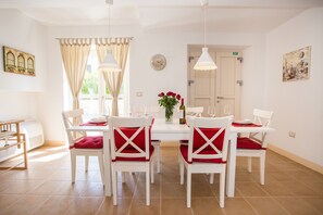 A dining area with a white table and chairs, a vase with red flowers, and a clock on the wall.