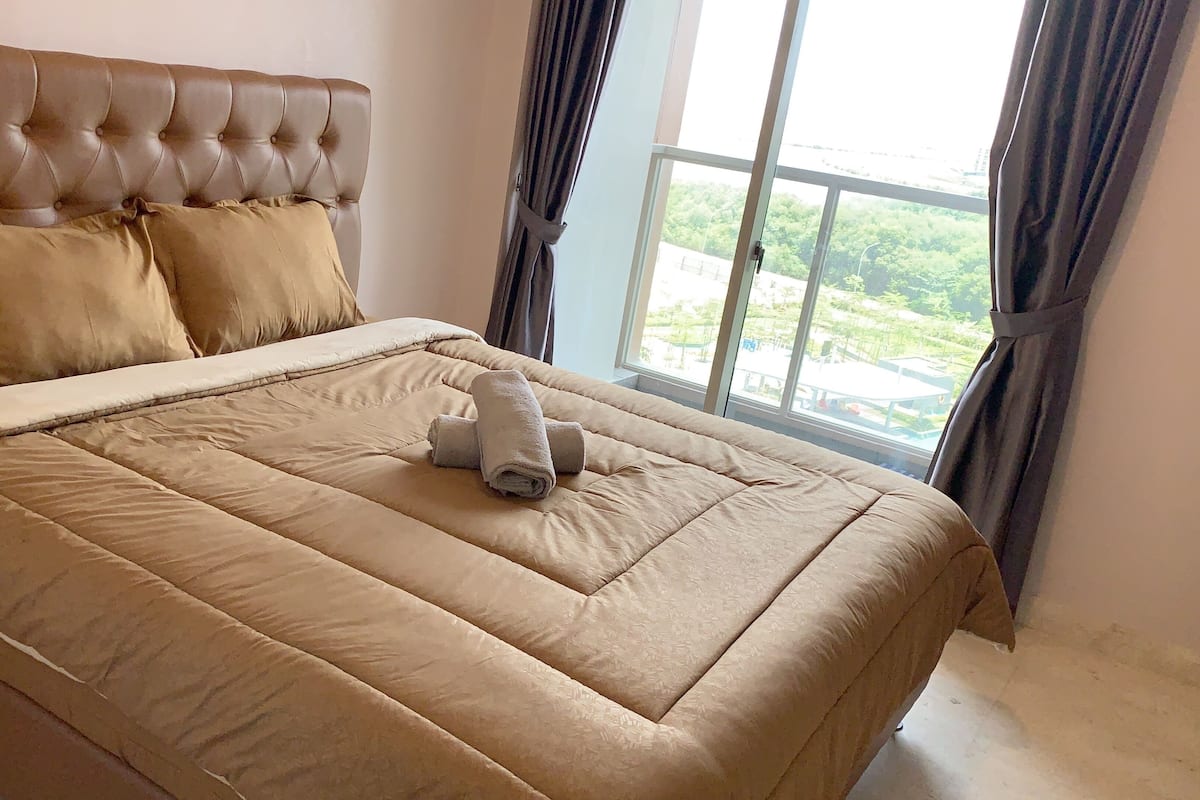 A bed with a tufted headboard, beige bedding, and a rolled towel on the bed.
