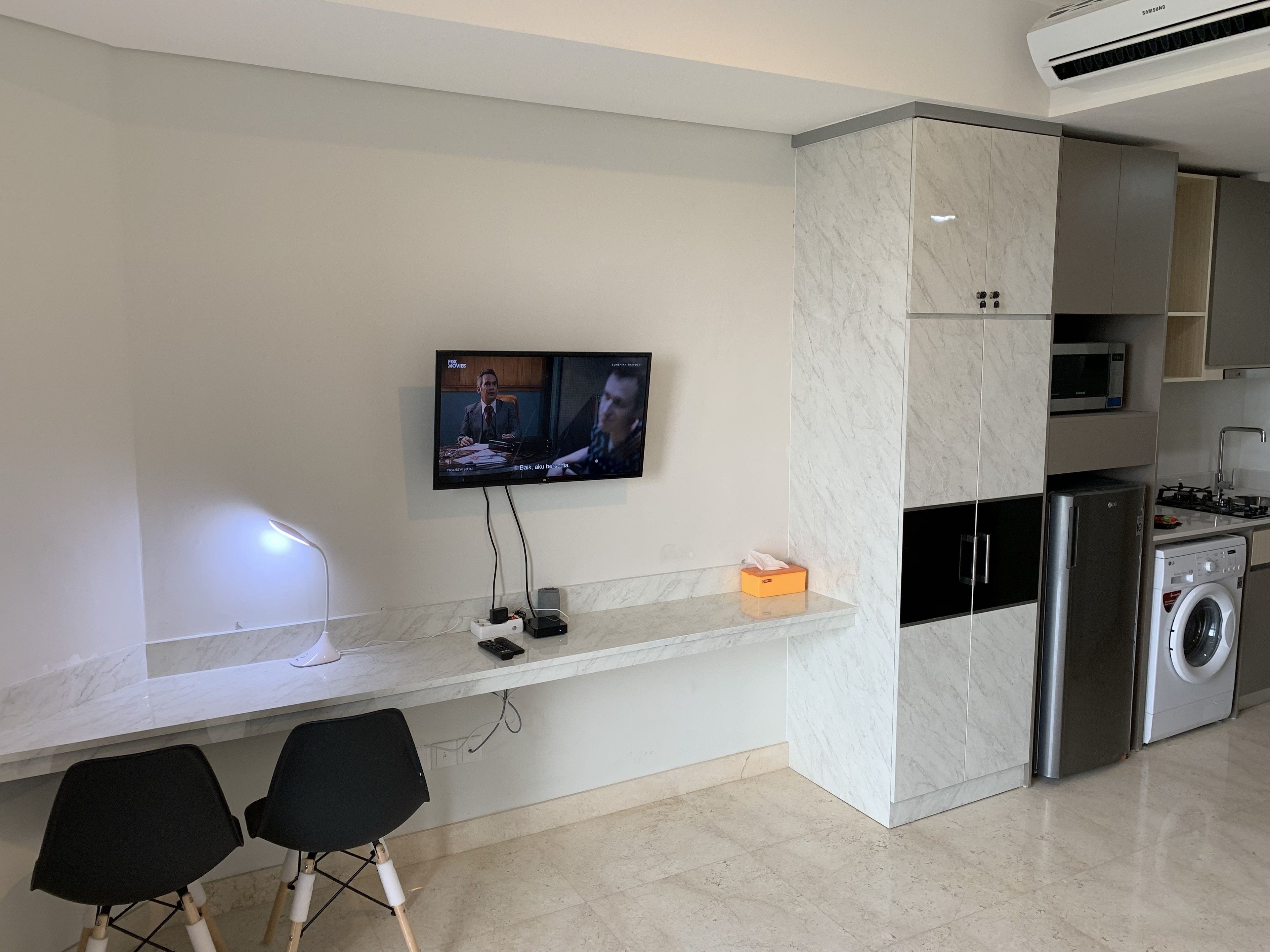 A modern kitchen with a built-in microwave, a washing machine, and a TV mounted on the wall.