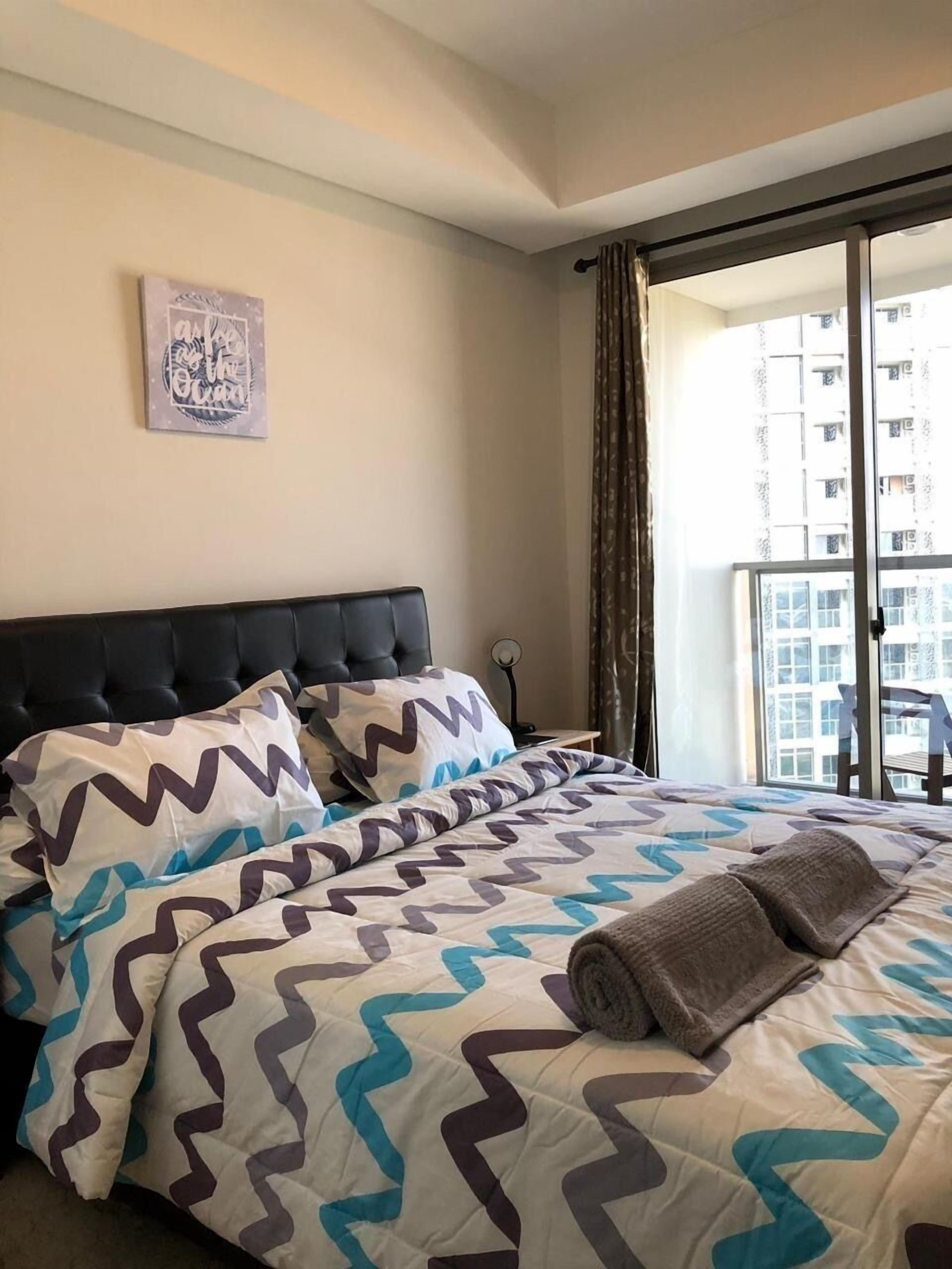 Camera d'albergo con un letto, un comodino, un quadro e un balcone con vista sugli edifici.